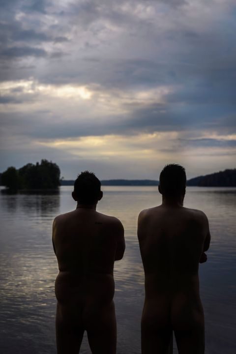 Miehet alasti selkä kameraan päin katsomassa järvelle iltahämärässä